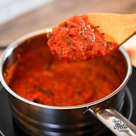 low carb pizza sauce shown on a wooden spoon over a metal pan